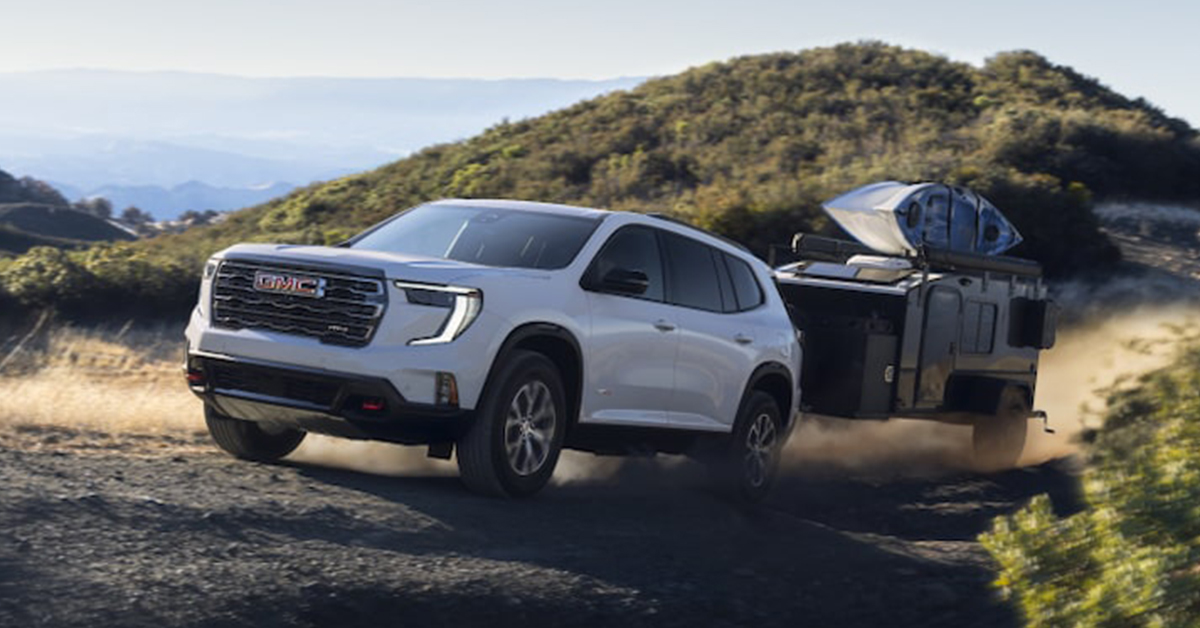 2025 GMC Acadia driving uphill while towing a small trailer